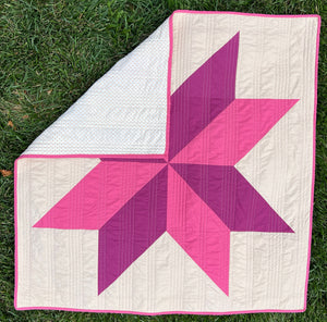 Image of a pink and purple handmade quilt for sale. A wonderful handmade gift for baby or a new mom. The top half of the quilt is folded over to see the backing fabric.