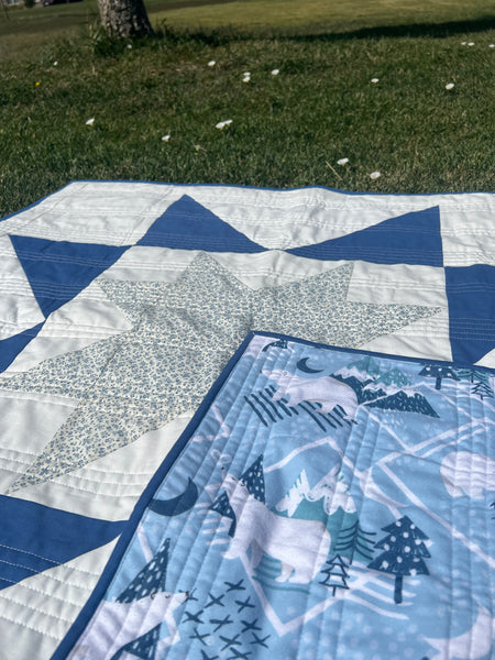 Image of a handmade baby quilt for sale. This quilt for sale is blue and white with a floral star and is backed with a winter themed flannel. 