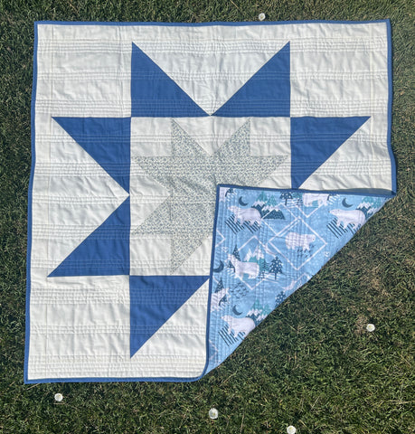 Image of Nemo and Stitch's handmade baby quilt for sale. Photographed with one corner flipped up to see the backing fabric. This quilt for sale is blue and white with a floral star and is backed with a winter themed flannel. Perfect baby gift, nursery decor, etc. 